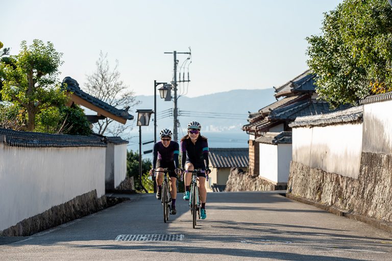 日出城下町を笑顔で走るサイクリストカップル